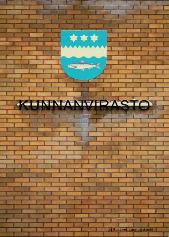 Kuvassa kunnanviraston sivuseinä, jossa vaakuna ja rakennuksen nimi kirjoitettuna